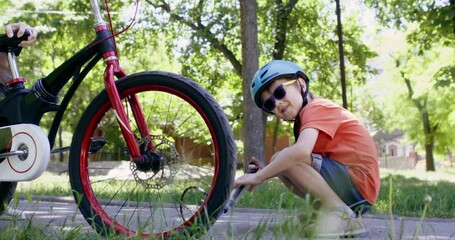 Preschooler child in sunglasses inflates bicycle tire in park. Skillful boy checks whether tire inflated sufficiently and keeps pumping with hand