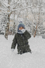 A little boy is playing in the snow outside in the park, snowball games, sculpting a castle out of snow, games in the snow, climate change, happy moments outdoors.