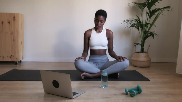 African American woman doing yoga stretching exercices at home using laptop. 4k resolution video.