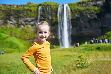 Adorable preschooler girl having fun near waterfall Seljalandsfoss in Thingvellir National Park, Iceland.