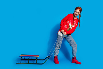 Full length photo of lovely young lady pull sledge dressed red christmas garment celebrate winter holidays on blue color background