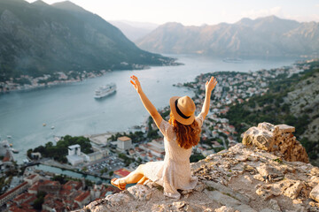 A joyful woman enjoys the stunning view of Kotor Bay from a mountain overlook on a sunny day in Montenegro. Europe travel. Lifestyle, vacation, tourism, nature, active life.