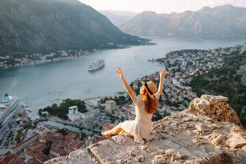 A joyful woman enjoys the stunning view of Kotor Bay from a mountain overlook on a sunny day in Montenegro. Europe travel. Lifestyle, vacation, tourism, nature, active life.