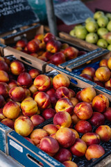 Vibrant peaches, with their striking red and yellow skin, are artistically arranged in wooden crates at a lively farmer's market, enticing visitors with their freshness and beauty.