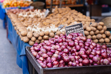 A bustling market scene filled with fresh vegetables, including vibrant red onions and earthy potatoes, inviting visitors to explore the local produce offerings in a lively atmosphere.