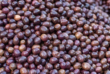 A vibrant collection of freshly harvested olives is displayed at a bustling market, their rich hues glistening under the warm sun, inviting passersby to explore their unique flavors.