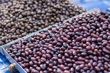 Baskets filled with plump, glistening olives showcase a variety of rich colors, tempting shoppers at a lively Mediterranean market. The atmosphere is filled with enticing aromas.
