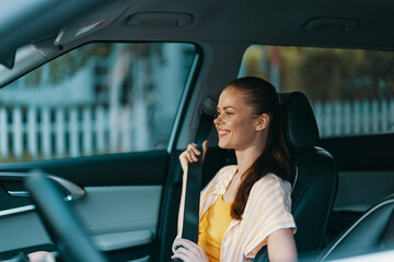 Smiling young woman in a car, enjoying the moment with a relaxed expression, wearing a yellow dress and light striped shirt, with a blurred background of a sunny day