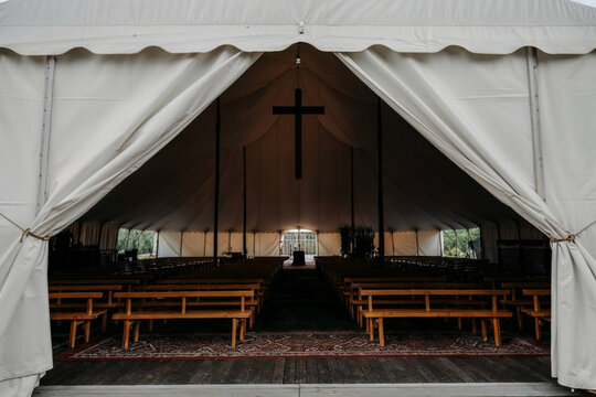 White church tent with wooden benches arranged in rows, featuring a corridor leading to the altar. Commonly used for Christian revivals, worship services, evangelism, and faith-based gatherings.
