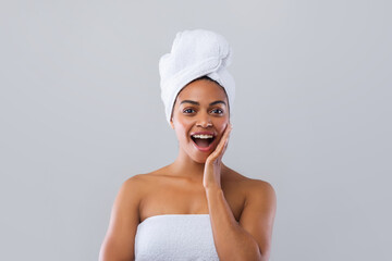 Excited black woman wrapped in towels touching her cheek, shocking deals for spa procedures