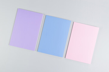 Top view of pink, purple and blue notebooks on grey background. School, office wallpaper. Flat lay, copy space.