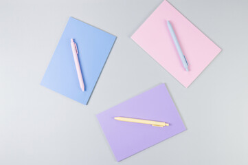 Top view of pink, purple and blue notebooks on grey background. Pink, yellow and blue pens, school, office wallpaper. Flat lay, copy space.