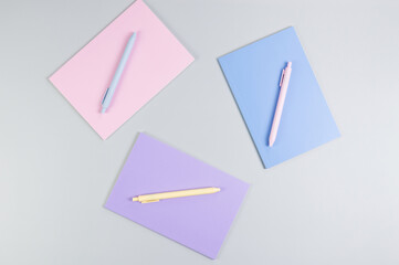 Top view of pink, purple and blue notebooks on grey background. Pink, yellow and blue pens, school, office wallpaper. Flat lay, copy space.