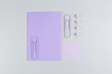Top view of purple notebook on grey background. Purple sticky note, paperclips and pins. School, office wallpaper. Flat lay, copy space.
