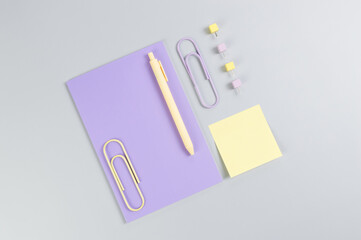 Top view of purple notebook on grey background. Sticky note, paperclips, pen and pins. School, office wallpaper. Flat lay, copy space.