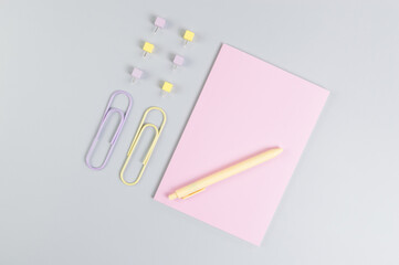 Top view of pink notebook on grey background. Paperclips, pen and pins. School, office wallpaper. Flat lay, copy space.