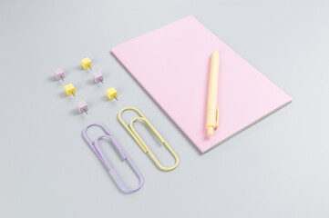 Top view of pink notebook on grey background. Paperclips, pen and pins. School, office wallpaper. Flat lay, copy space.
