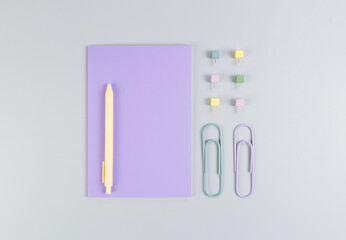 Top view of purple notebook on grey background. Paperclips, pen and pins. School, office wallpaper. Flat lay, copy space.