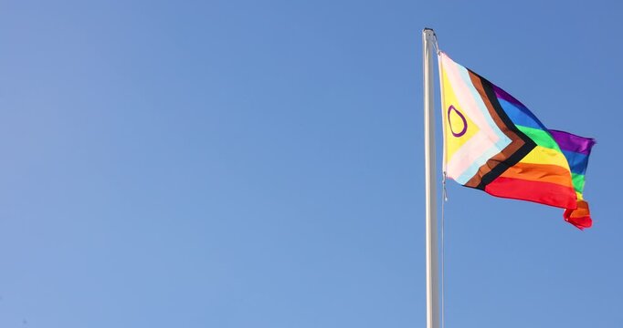 LGBTIQ flag waving on a background of blue sky of a sunny day. 