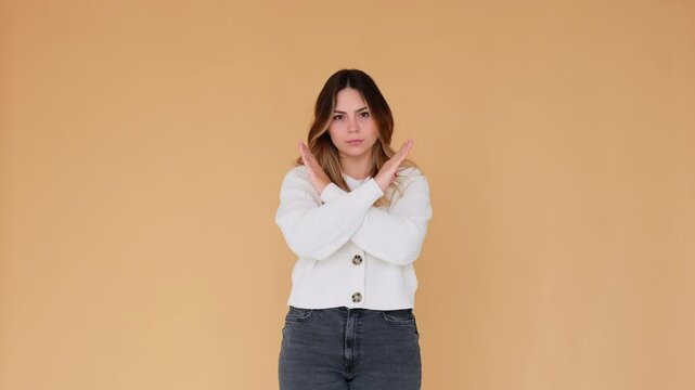 Serious and stern Caucasian young woman crossing arms in stop sign on beige background. Prohibition, protest and protection concept.