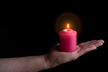 Outstretched man's hand holding a lit red candle against black background