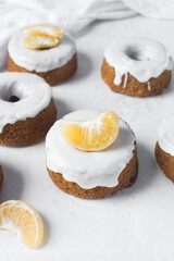Iced mini bundt cake on a white tray, vanilla bundlette cakeswith a clementine segment on a white background, small vanilla bundt cakes with an icing glaze