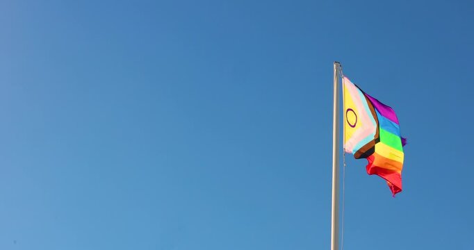 LGBTIQ flag waving on a background of blue sky of a sunny day. 