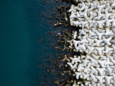 Heavy concrete tetrapods lined along the shoreline at a coastal area during daylight hours