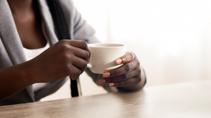 Unrecognizable afro businesswoman drinking coffee and using laptop in office, crop