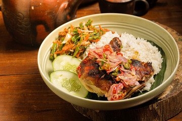 Close up red chili grilled chicken rice on white bowl. spicy and savory dish, sliced ​​cucumber and assorted vegetables we usually called urap. perfect for menu, catalogue or commercial use