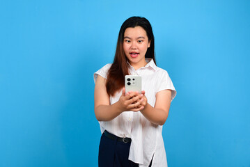 Surprised Asian woman looking at her smartphone over blue background with copyspace