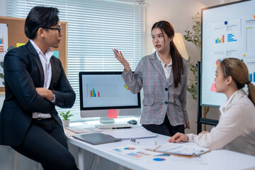 Three people are sitting at a desk with a computer monitor in front of them