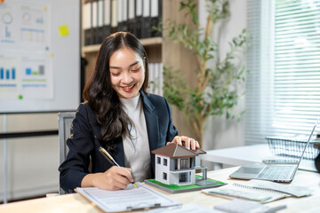 A woman is sitting at a desk with a house model in front of her