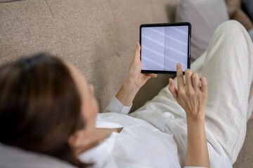 A woman is laying on a couch and using a tablet