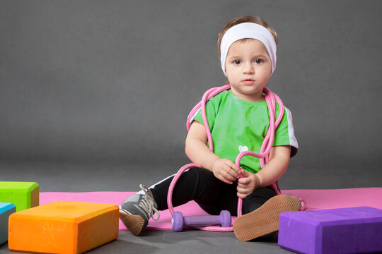 Two year old girl doing sports posing with skipping rope and ball on grey background.Sports activities with little kids.