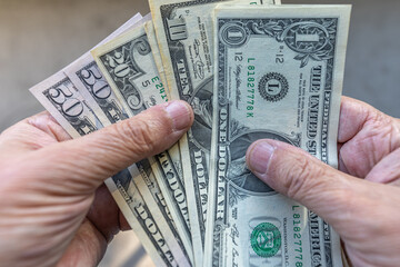 Close-up of US dollar bills being counted on a man's hands, against plain grey background, in denominations going from one to fifty dollar bills. 