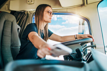 Portrait of beautiful young woman professional truck driver sitting and driving big truck. She is...