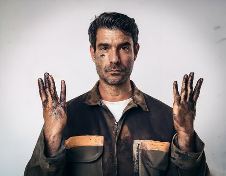 A mechanic specializing in vehicle and engine repair is portrayed with his hands and face smeared with grease, set against an isolated gray background.