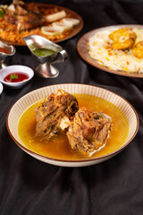 clear mutton soup on a brown plate, served with chili sauce and gravy. Isolated from dark background. Perfect for menu, catalogue, advertising or commercial use