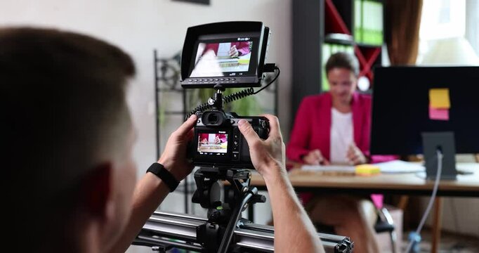 The operator with a digital camera shoots a business woman at the table. Concept video filming in the office