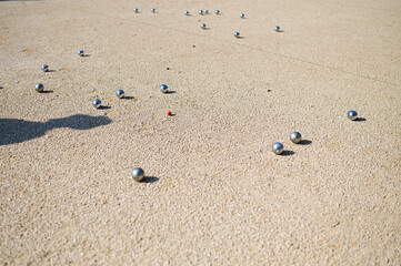 Close-up of petanque balls scattered on gravel with the target ball in focus. The shiny metal balls reflect sunlight, capturing a playful outdoor moment in a park setting