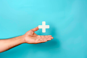 Male hand holding plus icon on blue background. Plus sign virtual means to offer positive thing like benefits, personal development, social network Profit,health insurance, growth concepts