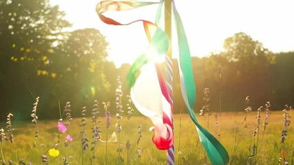 Static video of a maypole during beltane in a sunlit meadow, with colorful ribbons fluttering in the breeze