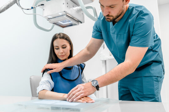 Male doctor works with an x-ray machine in a modern hospital while patient sitting on special sit. Radiologist takes a picture of the arm. The concept of medical technologies, modern medical equipment