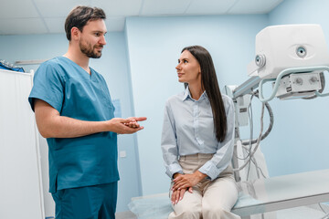 Medical worker specialist is talking to patient. Male radiologist is standing near patient woman...