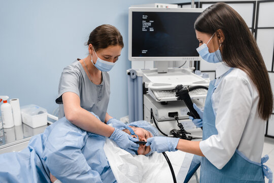 Team of female doctor and nurse assistant performing gastroscopy in hospital, examining stomach of young male patient in modern clinic cabinet hospital. Gastroscopy procedure concept