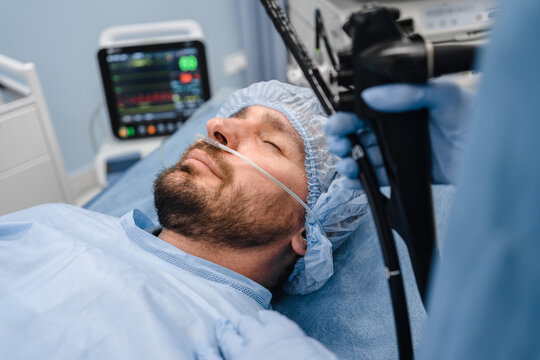 Male patient lying on the operating table under anesthesia with monitor screen for emergency heart pump, doctor holding modern endoscope device before gastroscopy colonoscopy examination
