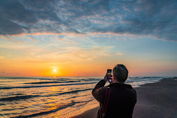 A traveler on the beach captures a colorful sunrise on his smartphone