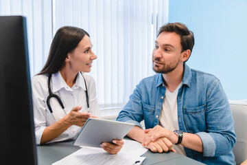 Portrait of male patient in medical office listening to a friendly female doctor holding report file with appointment and giving consultation a man during medical examination in clinic.