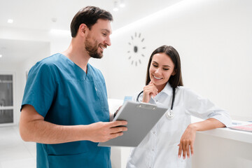 Beautiful young doctors are working with documents and smiling while standing in hospital hall. Medical group talking about support strategy, medicine and surgery teamwork in hospital